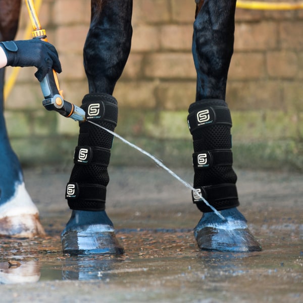 Horse being washed with a hose, wearing black Coolboot leg wraps with StreamZ brand logo.