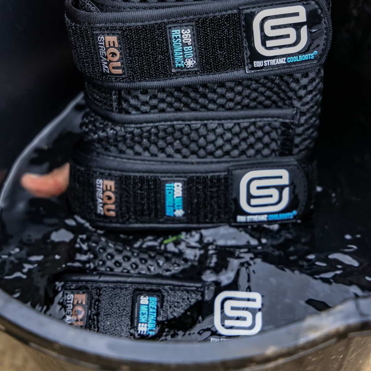 Stack of black EQU STREAMZ cool boots in bucket of cold water for cooling